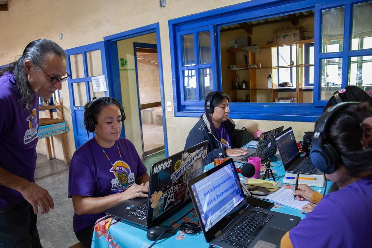 Community radio participants work with laptops, headphones and microphones.