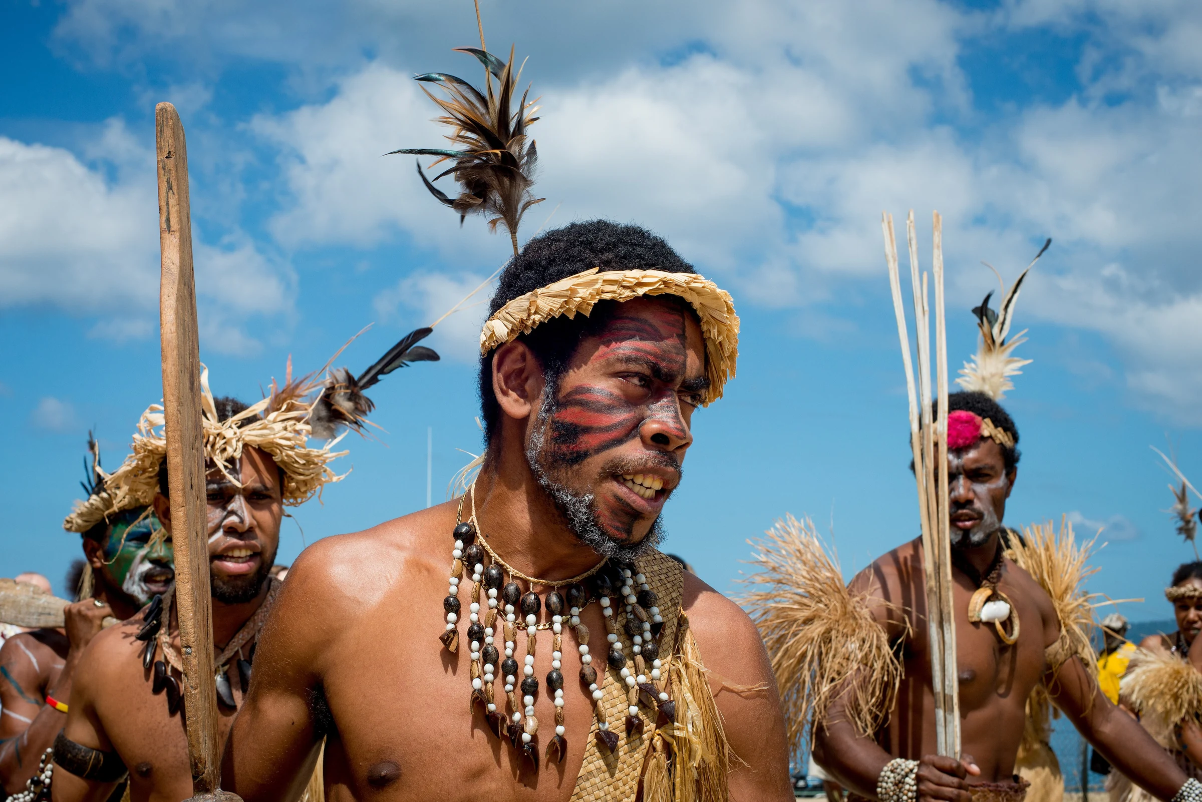 Futuna performers wearing traditional adornments stand against a blue sky.